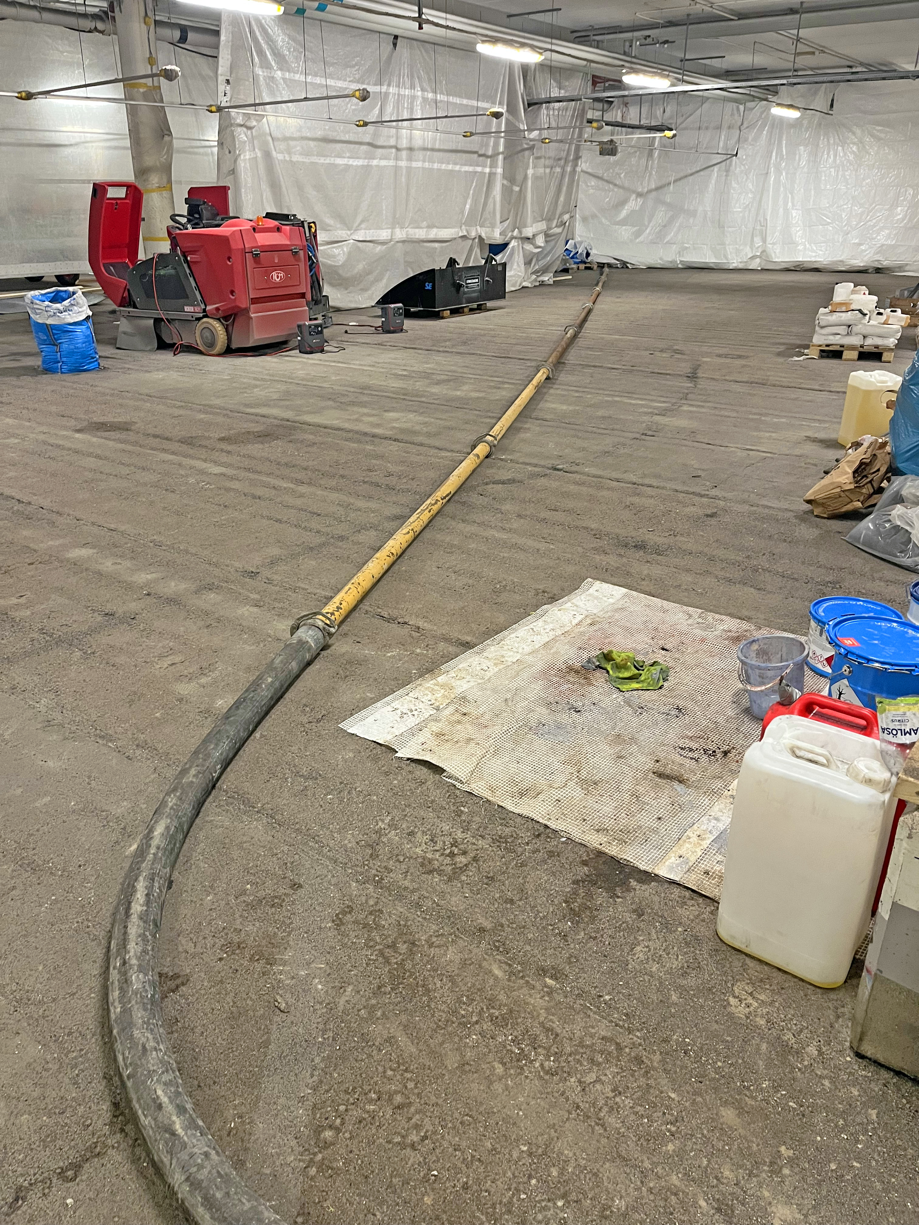 Parkeringsgarage med en lång slang på golvet, omgiven av utrustning och material.
