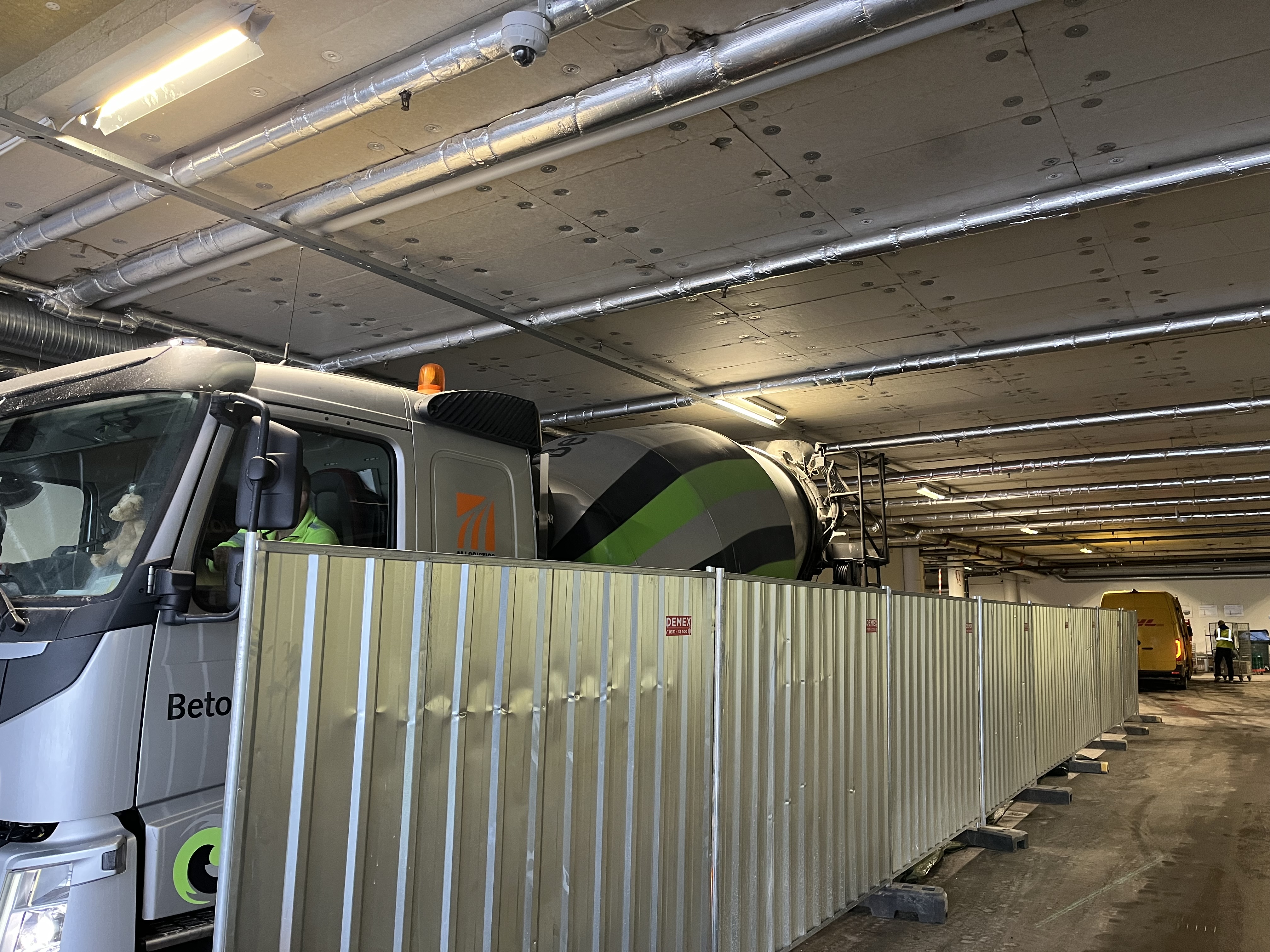 Betonglastbil arbetar i ett parkeringsgarage bakom en metallavspärrning.