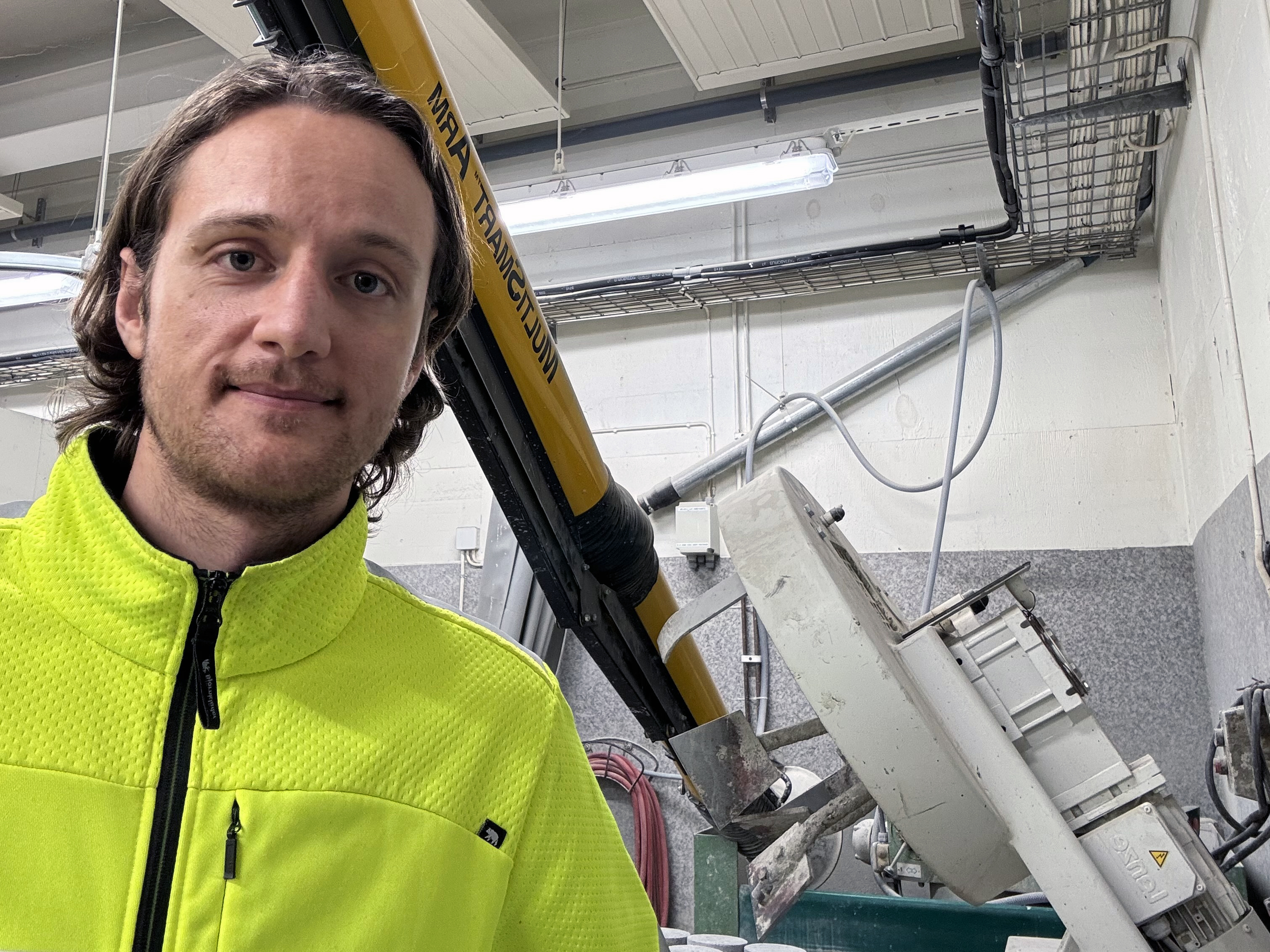 Person i gul arbetsjacka står nära industriell utrustning inomhus.