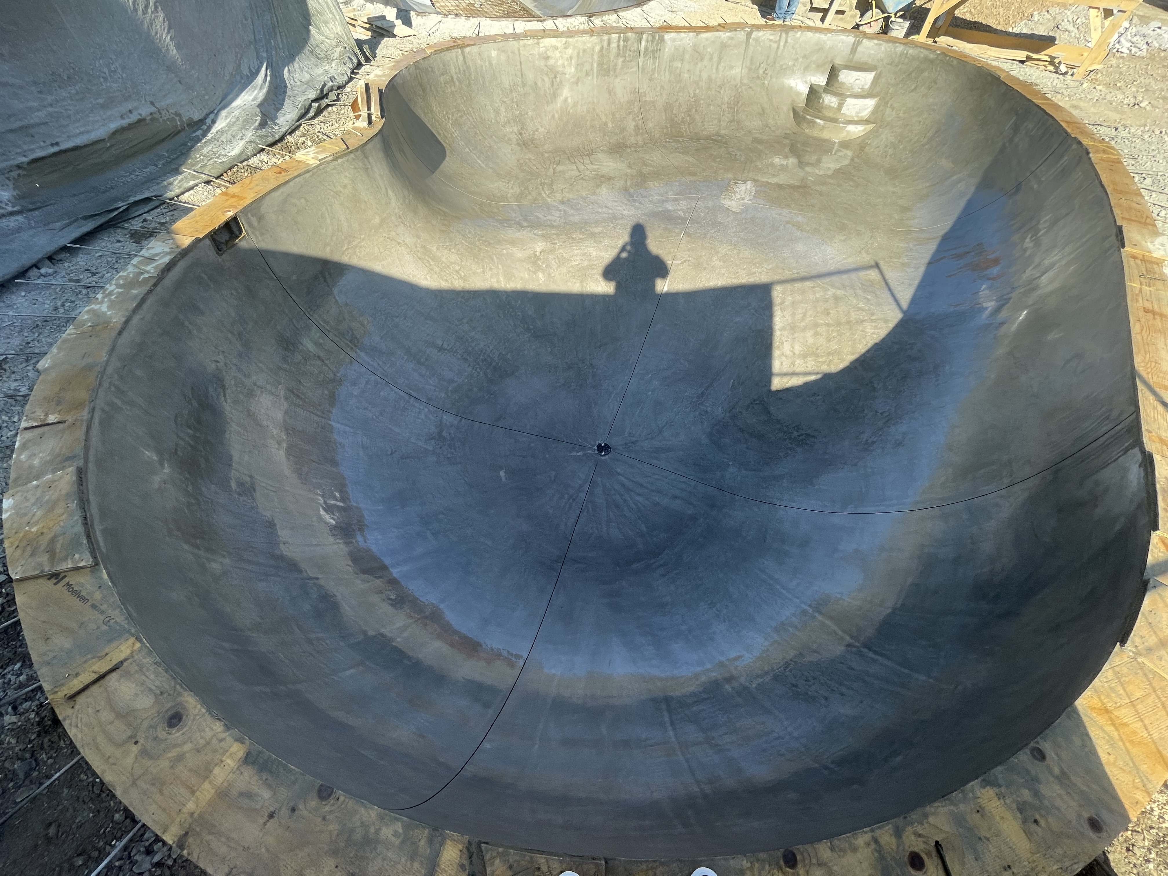 Skateramp i betong under konstruktion med en skugga av en person i centrum.