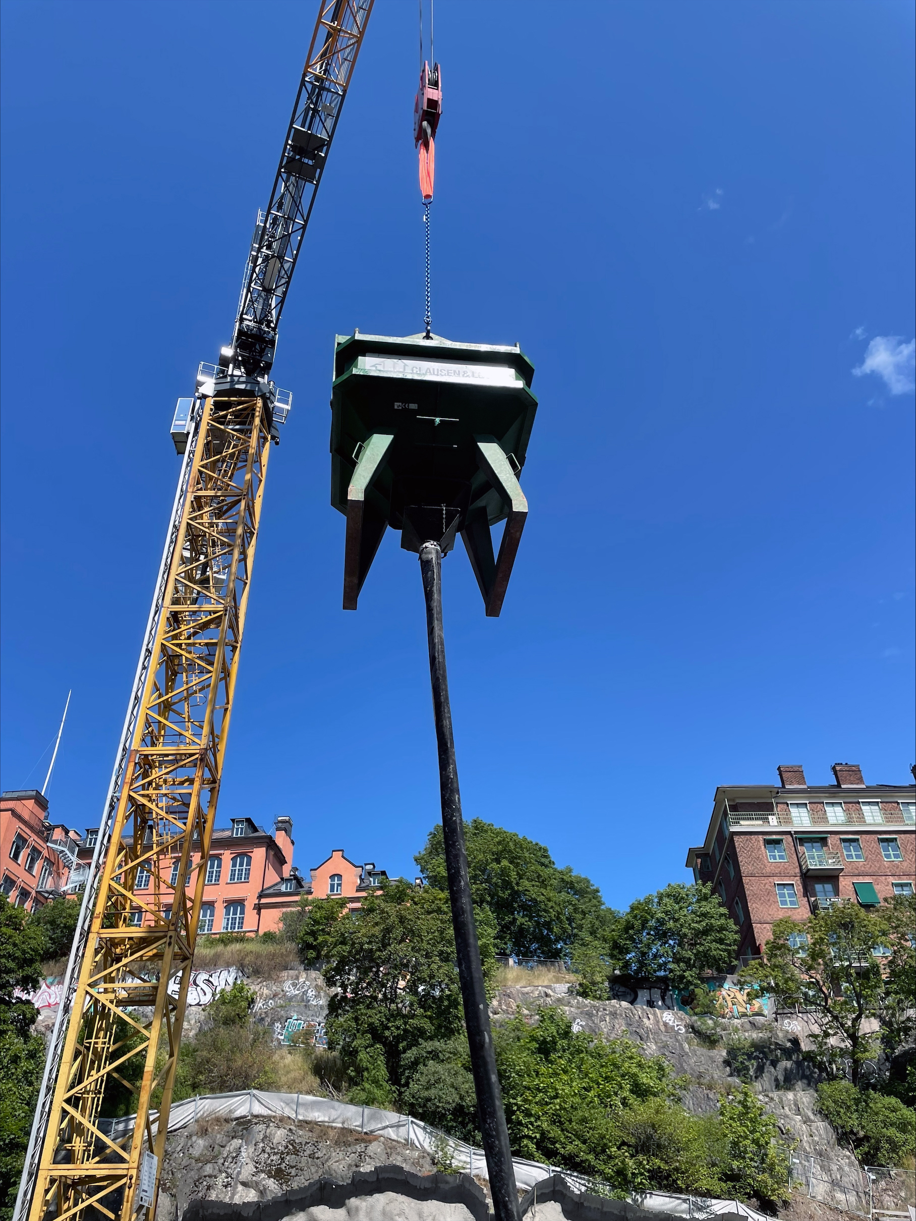 En byggkran lyfter en stor kask på en byggarbetsplats med bostäder i bakgrunden.
