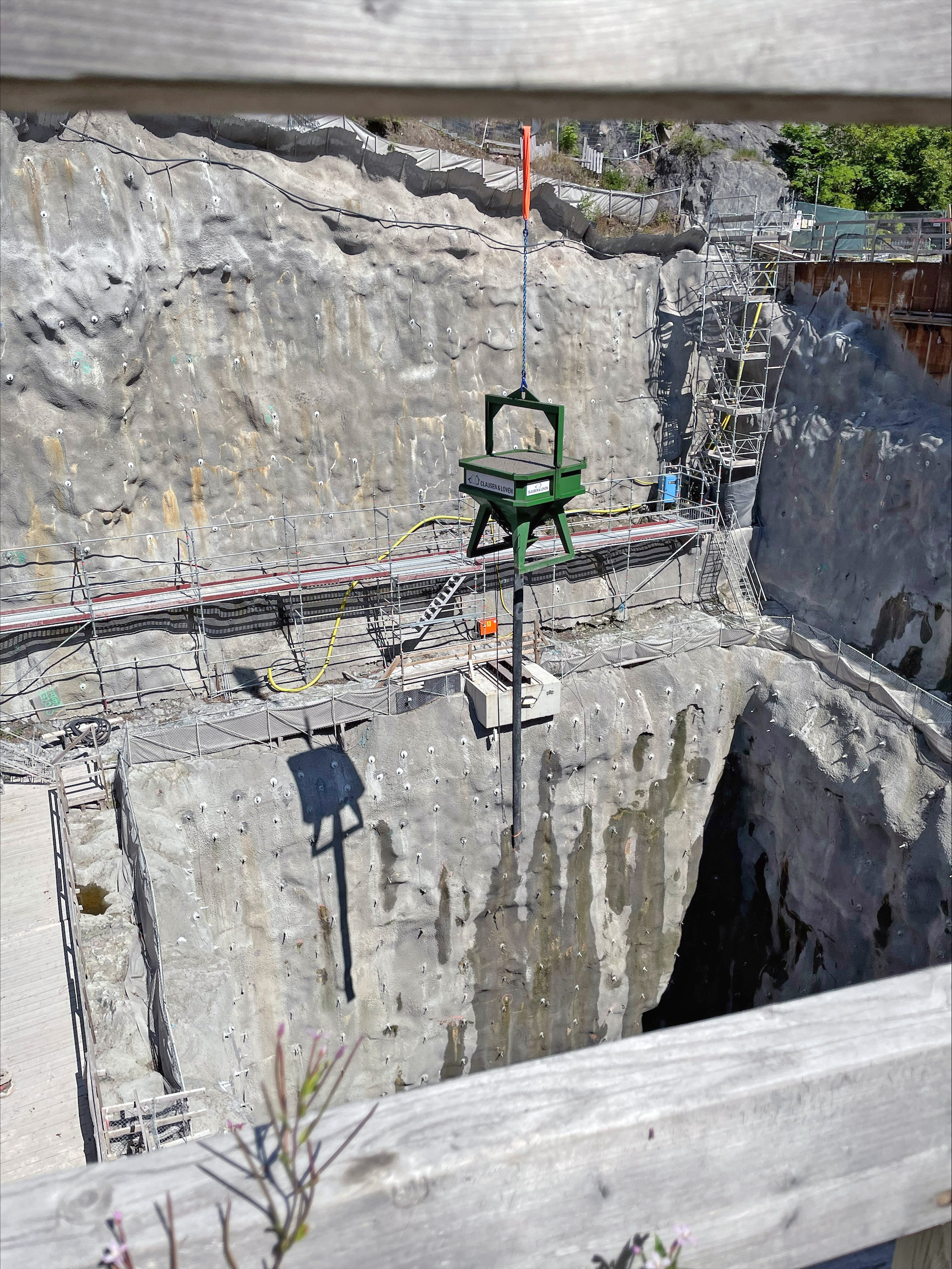 En byggarbetsplats där en kask med betong lyfts över ett hissschakt.