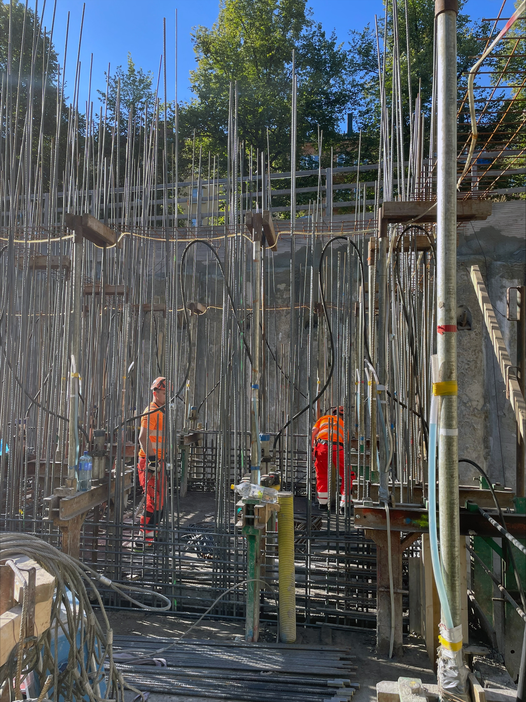 Byggarbetsplats med arbetare i orange arbetskläder omgivna av armeringsjärn.