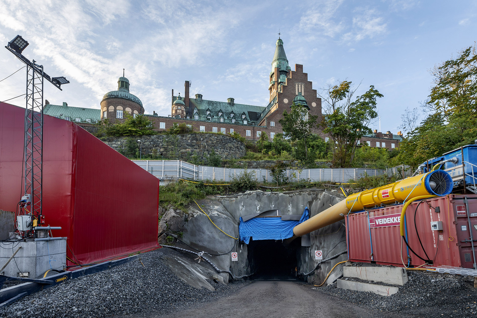 Ingången till en tunnel på en byggarbetsplats med en historisk byggnad i bakgrunden.
