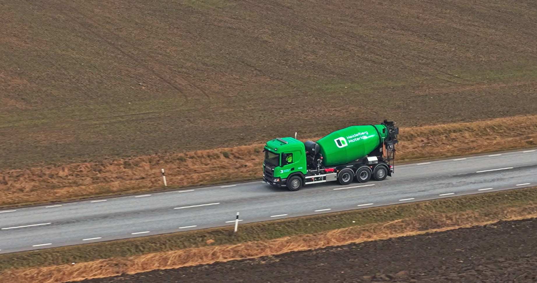 En betonglastbil från Heidelberg Materials kör på en landsväg omgiven av åkermark.