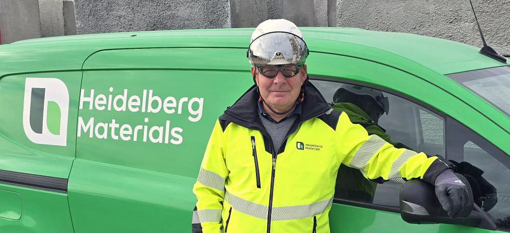 En person i arbetskläder står framför ett grönt fordon med Heidelberg Materials-logotypen.