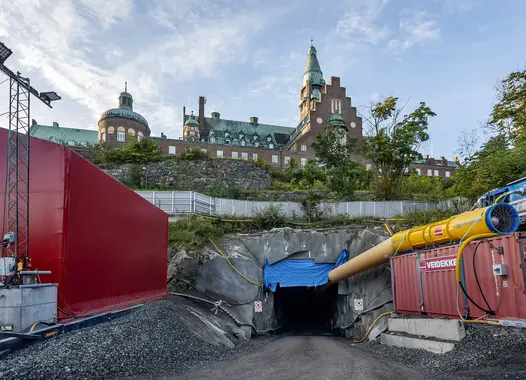 Ingången till en tunnel på en byggarbetsplats med en historisk byggnad i bakgrunden.